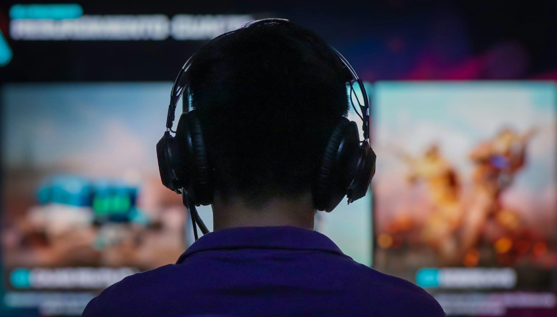 A person wearing a headset in front of a screen displaying a video game.